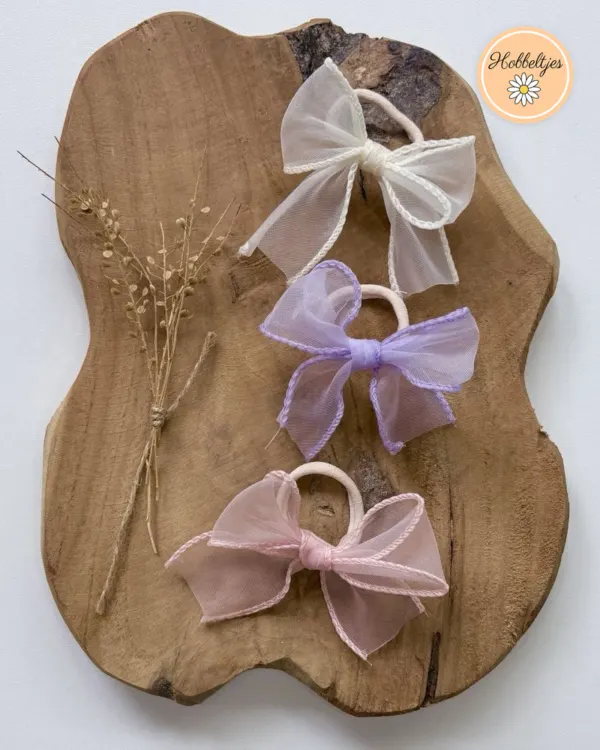 Drie haarelastieken met een organza strik in wit, lila en roze